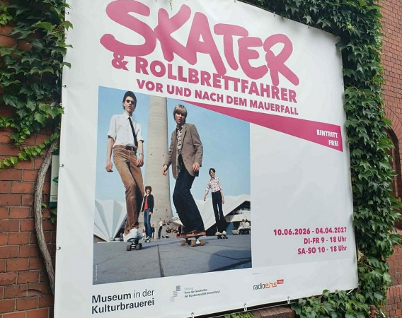 Plakat wystawy, na nim kilku jadących na deskorolkach