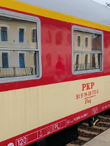 Biało-beżowy wagon starego składu pociagow PKP. Ma duże okna. Stoi na peronie.