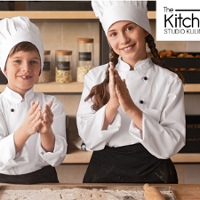 Dwoje dzieci w strojach kucharza w kuchni. Logo studia kulinarnego.