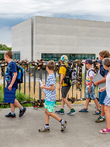 Grupa dzieci wchodzi na most, w tle widać prostopadłościenny, szary budynek Bramy Poznania.