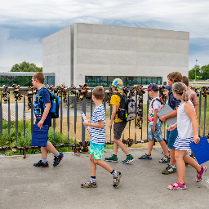 Grupa dzieci wchodzi na most, w tle widać prostopadłościenny, szary budynek Bramy Poznania.