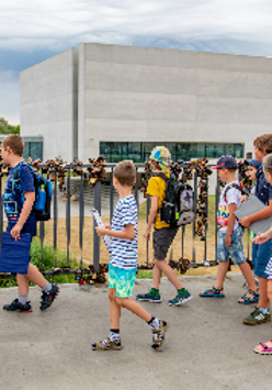 Grupa dzieci wchodzi na most, w tle widać prostopadłościenny, szary budynek Bramy Poznania.