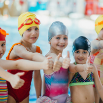 Grupa dzieci w strojach pływackich i czepkach stoi na basenie.