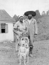 Stara, czarno-biała fotografia, a na niej kobieta, mężczyzna i trójka dzieci pozują przed domem.