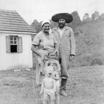 Stara, czarno-biała fotografia, a na niej kobieta, mężczyzna i trójka dzieci pozują przed domem.