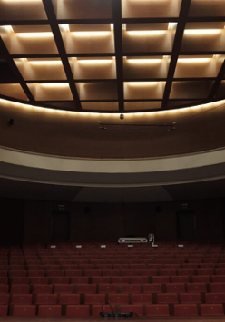 Obrazek przedstawia ciemną aule z czerwonymi krzesłami