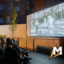 Zdjęcie, osoby w słuchawkach na uszach siedzą przed dużym ekranem na dachu kina.