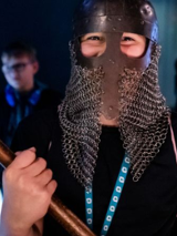 Osoba w wikińskim hełmie trzyma w obu dłoniach lekki toporek bojowy.