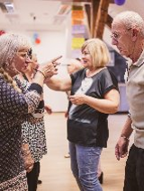 Grupa seniorów stoi w pomieszczeniu i rozmawia.