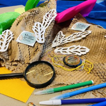 Na stole leżą różne przybory i akcesoria, w tym lupa i kolorowe mazaki.