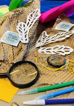 Na stole leżą różne przybory i akcesoria, w tym lupa i kolorowe mazaki.