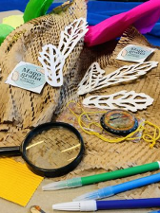 Na stole leżą różne przybory i akcesoria, w tym lupa i kolorowe mazaki.