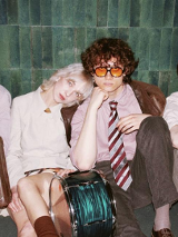 Kilka mlodych osób siedzi oparta o ścianę, oświetlona mocnym, białym światłem.