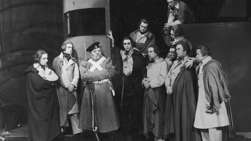Archiwalne, czarno-białe zdjęcie aktorów grających na scenie.