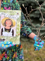 Ogrodniczka w jednej ręce trzyma książkę a w drugiej gałązki.