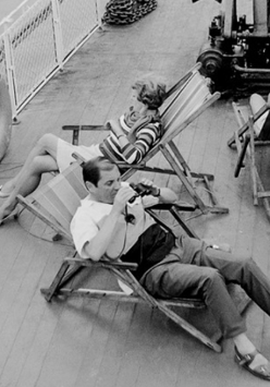 Kadr przedstawia dwie osoby, kobietę i mężczyznę, leżących na leżaczkach na pokładzie statku wycieczkowego. Patrzymy na nich z lotu ptaka.