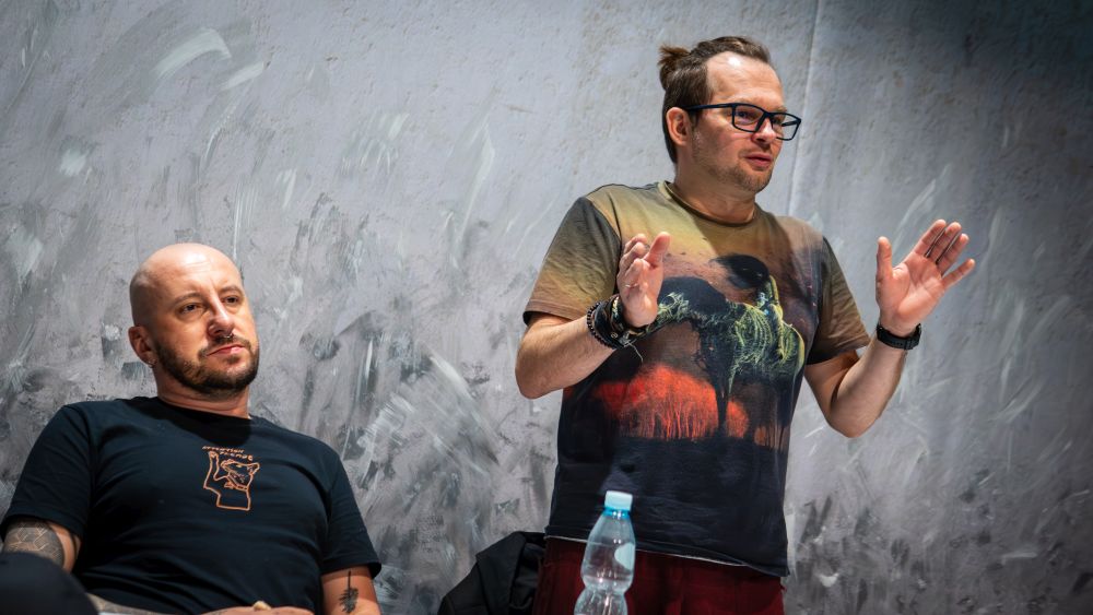 Reżyser stoi przy stole, referując coś.