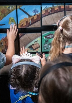 Grupa dzieci w słuchawkach dotyka kolorowej, interaktywnej wystawy w muzeum.