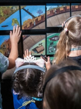 Grupa dzieci w słuchawkach dotyka kolorowej, interaktywnej wystawy w muzeum.