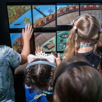 Grupa dzieci w słuchawkach dotyka kolorowej, interaktywnej wystawy w muzeum.