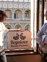 Zdjęcie dwóch mężczyzn, jeden w stroju kucharza, drugi trzyma szyld Rogalowego Muzeum Poznania