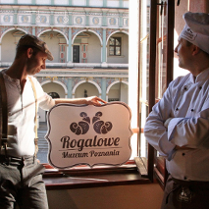 Zdjęcie dwóch mężczyzn, jeden w stroju kucharza, drugi trzyma szyld Rogalowego Muzeum Poznania