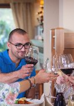 Zdjęcie, grupa osób siedzi przy wspólnym stole i stuka się kieliszkami z winem.