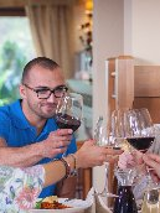 Zdjęcie, grupa osób siedzi przy wspólnym stole i stuka się kieliszkami z winem.