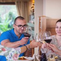 Zdjęcie, grupa osób siedzi przy wspólnym stole i stuka się kieliszkami z winem.