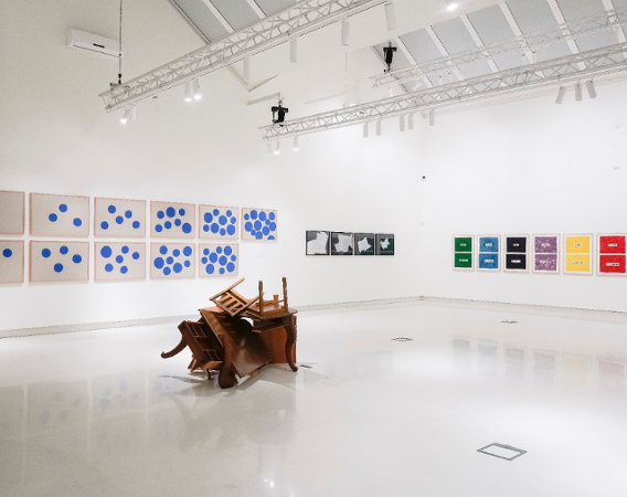 Rzeźba ułożona z krzeseł i obrazy na ścianach galerii