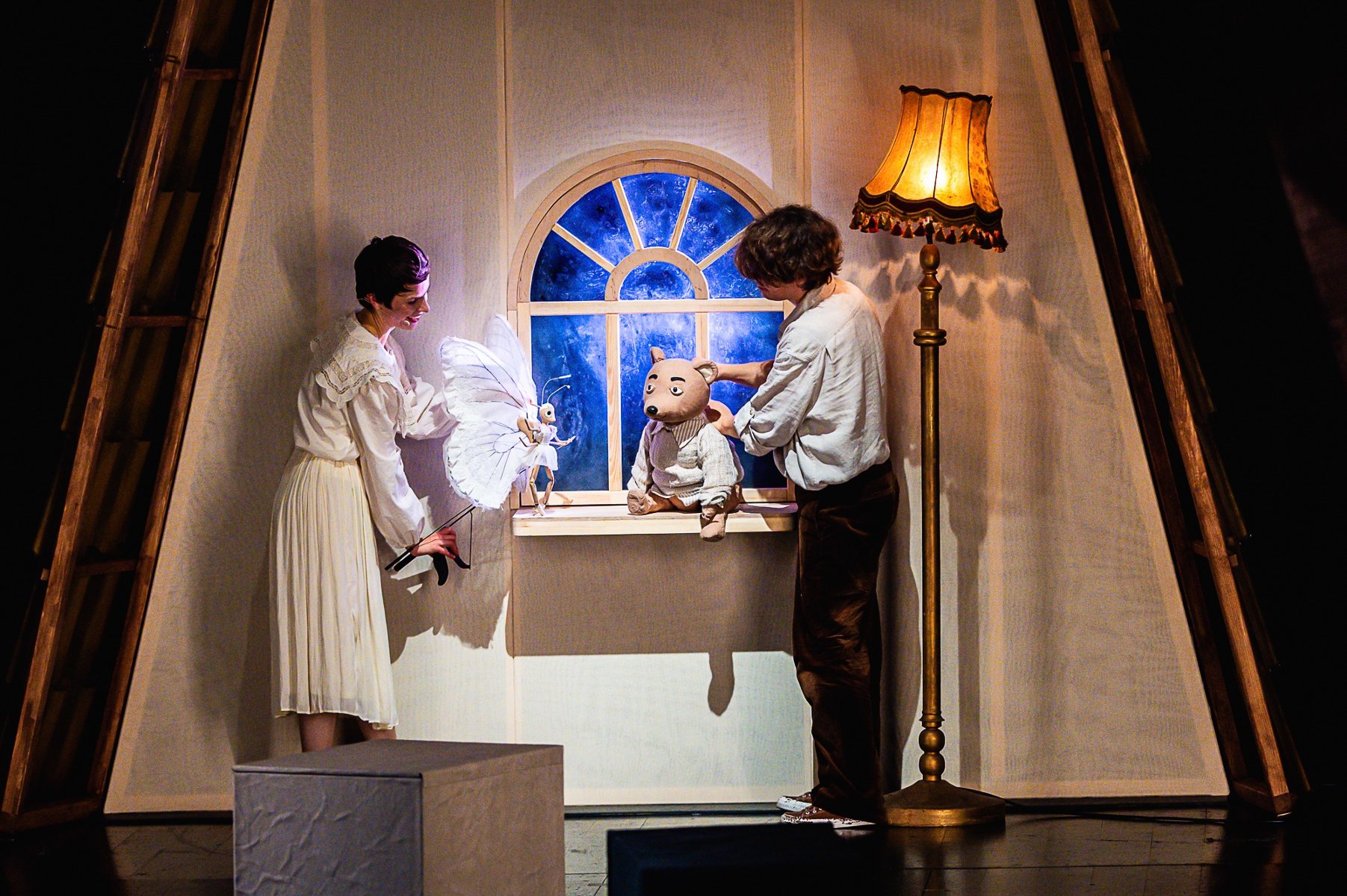Scena ze spektaklu. Dwoje aktorów animuje lalki - niedźwiedzia i motyla. Niedźwiedź siedzi na oknie.