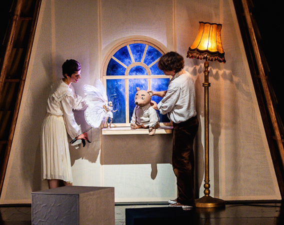 Scena ze spektaklu. Dwoje aktorów animuje lalki - niedźwiedzia i motyla. Niedźwiedź siedzi na oknie.