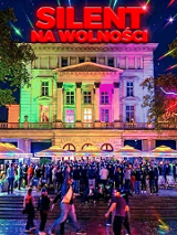 Oświetlony neonowymi lampkami plac Wolności pod budynkiem Arsenału. Na dachu budynku czerwony neon "Silent Na wolności". Pod budynkiem tłum ludzi.
