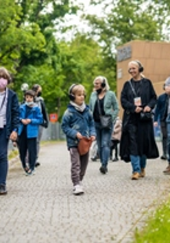 Zdjęcie przedstawiające grupę spacerujących ludzi ze słuchawkami na uszach.