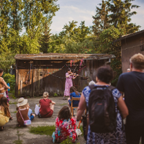 Tłum słucha kobiety grającej na skrzypcach na kameralnym podwórku domu.
