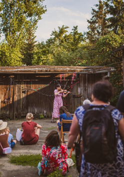 Tłum słucha kobiety grającej na skrzypcach na kameralnym podwórku domu.