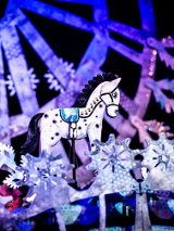 Zdjęcie ze spektaklu - biały drewniany konik wśród dekoracji w bialo-fioletowych kolorach.