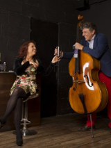 Zdjęcie ze spektaklu - kobieta siedzaca na stołku barowym, obok niej mężczyzna stojący przy kontrabasie.