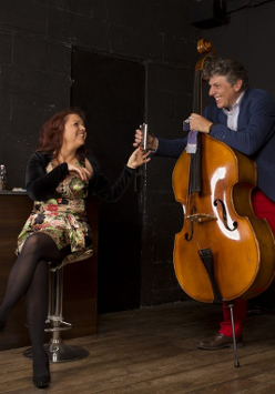 Zdjęcie ze spektaklu - kobieta siedzaca na stołku barowym, obok niej mężczyzna stojący przy kontrabasie.