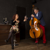 Zdjęcie ze spektaklu - kobieta siedzaca na stołku barowym, obok niej mężczyzna stojący przy kontrabasie.