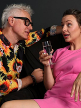 Zdjęcie ze spektaklu - kobieta z kieliszkiem w ręce naprzeciw wpatrzonego w nią mężczyzny.