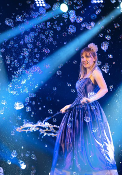 Zdjęcie z przedstawienia: kobieta w długiej, niebieskiej sukni wśród baniek mydlanych.