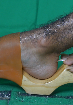 Zdjęcie owłosionej nogi pokrytej brokatem w drewnianym chodaku. Obok fragment drugiej stopy z długimi paznokciami.