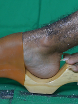 Zdjęcie owłosionej nogi pokrytej brokatem w drewnianym chodaku. Obok fragment drugiej stopy z długimi paznokciami.