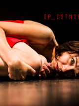 Zdjęcie ze spektaklu - kobieta w czerwonej sukience leży skulona na podłodze.