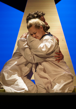 Zdjęcie ze spektaklu - kobieta i mężczyzna siedząc przytulają się do siebie.