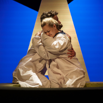 Zdjęcie ze spektaklu - kobieta i mężczyzna siedząc przytulają się do siebie.