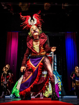 Zdjęcie ze spekatklu - na pierwszym planie aktor w stroju i masce, na drugim planie czterech aktorów.