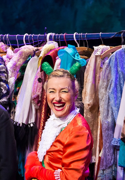 Zdjęcie ze spektaklu - aktorka w przebraniu do przedstawienia na tle wieszaka pełnego ubrań.