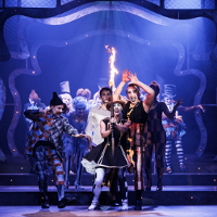 Zdjęcie ze spektaklu - grupa aktorów na scenie, na pierwszym planie aktorka trzymająca zapaloną pochodnię.